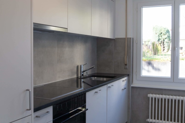 Cuisine après la rénovation d'un appartement à Pully près de Lausanne. Mobilier et carrelage gris