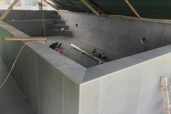 Détail d'un angles pour une piscine en carrelage à débordement. Image prise pendant les travaux avec protection contre les intempéries