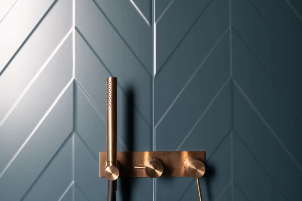 Détail d'un pommeau de douche dorée avec carrelage bleu. Maison à Rolle