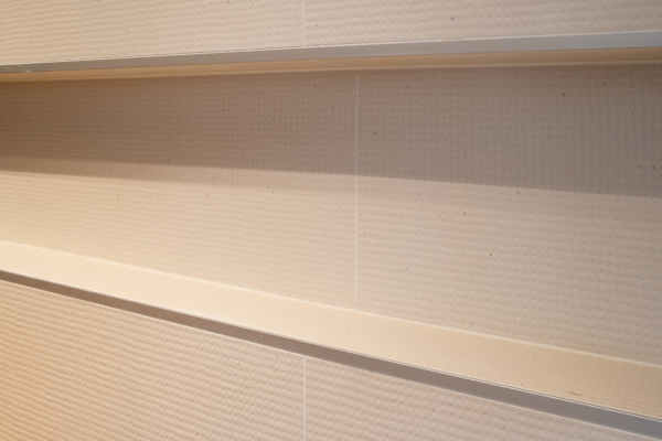 Un mur de carrelage beige texturé, avec des lignes épurées et des reliefs subtils, créant un effet moderne et élégant. Les séparations métalliques ajoutent une touche contemporaine, parfaite pour une salle de bains ou une cuisine, apportant à la fois style et fonctionnalité.