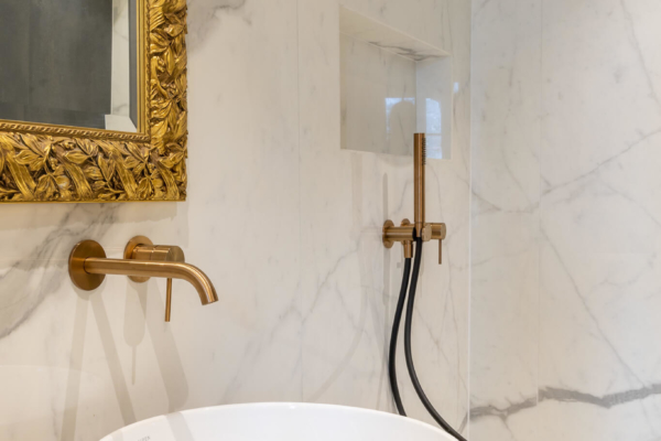 Lavabo blanc avec robinet doré et douche italienne en fond