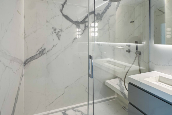 Vue d'une cabine de douche avec carrelage imitation marbre Calacatta de Graniti Fiandre, éclairée par un plafonnier rond à plusieurs ampoules, rénovée à Nyon.