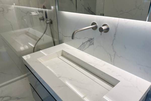 Lavabo moderne sur un comptoir avec carrelage imitation marbre Calacatta de Graniti Fiandre, avec robinetterie encastrée, dans une salle de bains à Nyon.
