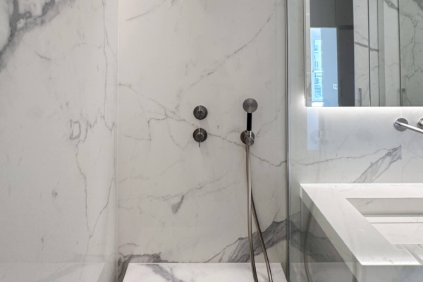 Intérieur d'une douche moderne avec carrelage imitation marbre Calacatta de Graniti Fiandre, portes en verre transparent, et étagères en verre, dans un appartement rénové à Nyon.