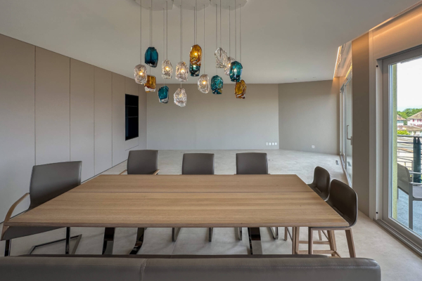 Salle à manger contemporaine avec carrelage imitation béton, table en bois massif et luminaires suspendus multicolores, rénovation à Nyon