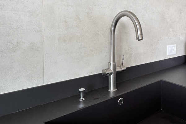 Lavabo moderne avec robinetterie en acier inoxydable, carrelage imitation béton en arrière-plan, appartement rénové à Nyon