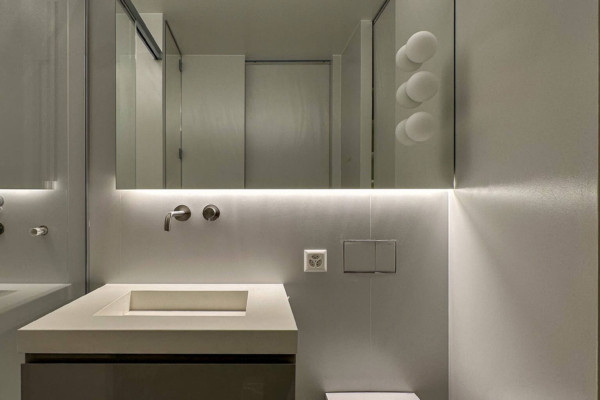 Salle de bains moderne après rénovation à Nyon, avec lavabo suspendu, murs texturés gris clair et éclairage LED encastré